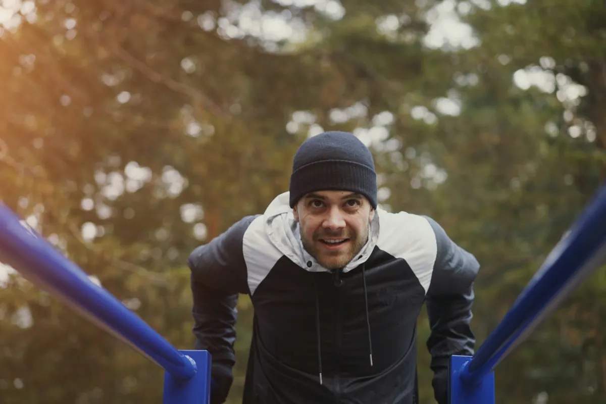 A man at the top of a dip on blue parallel bars in a park