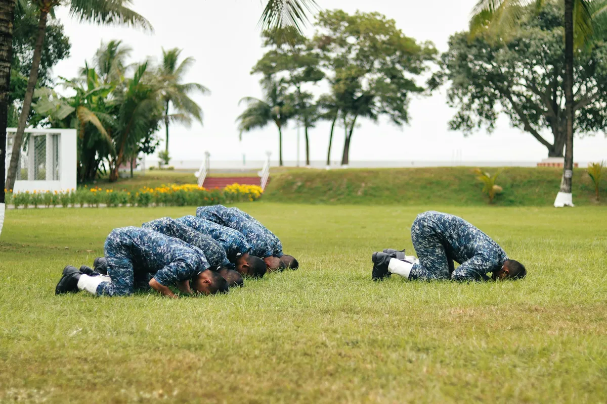 Uniformed personnel in camouflage holding the bottom of a push-up on a grass field