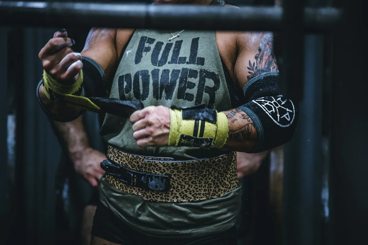 A close view of a lifter wearing a weight belt and wrist wraps, hands gripping a bar